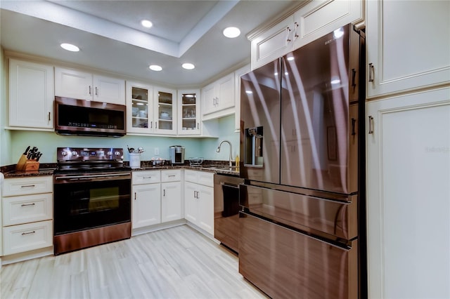 kitchen with light hardwood / wood-style flooring, appliances with stainless steel finishes, sink, white cabinets, and dark stone counters