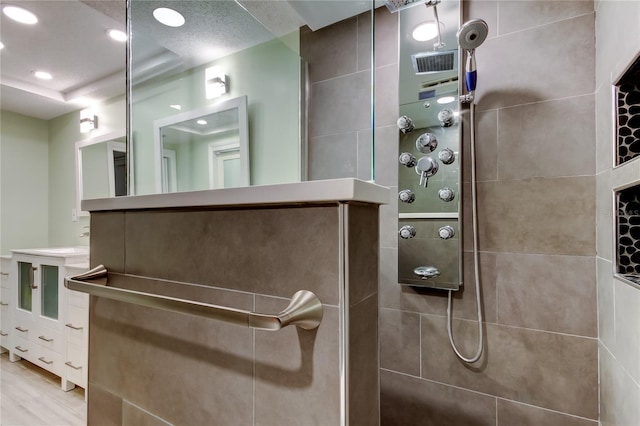 bathroom featuring hardwood / wood-style floors, tiled shower, vanity, and a raised ceiling