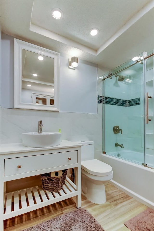 full bathroom featuring vanity, toilet, a raised ceiling, hardwood / wood-style flooring, and combined bath / shower with glass door