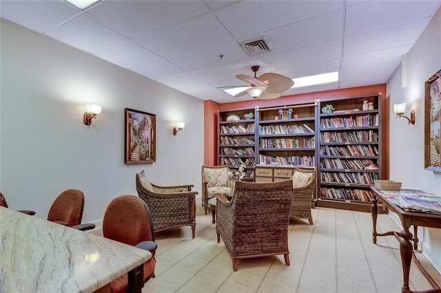 living area with built in shelves, a drop ceiling, and ceiling fan