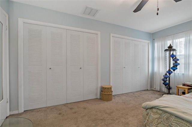 carpeted bedroom with ceiling fan and multiple closets