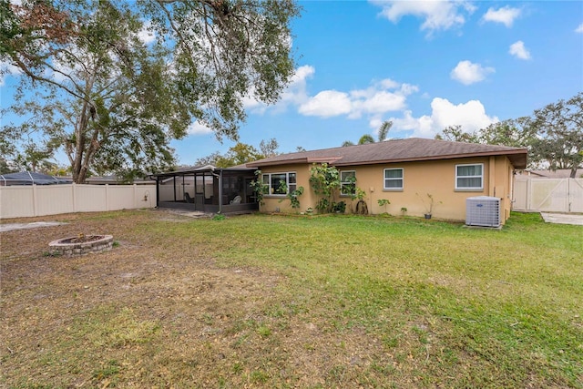 rear view of property featuring a lawn, an outdoor fire pit, cooling unit, and a sunroom