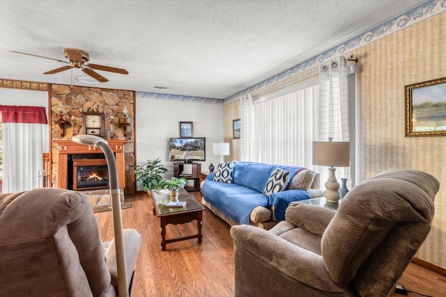 living room featuring a textured ceiling, ceiling fan, a large fireplace, and hardwood / wood-style flooring