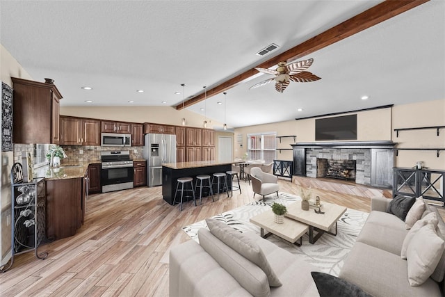 living room featuring a stone fireplace, lofted ceiling with beams, light wood-type flooring, ceiling fan, and visible vents