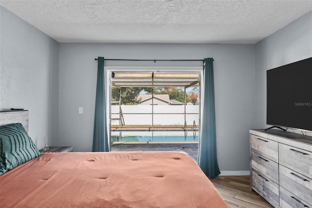 bedroom with light wood finished floors, baseboards, and a textured ceiling