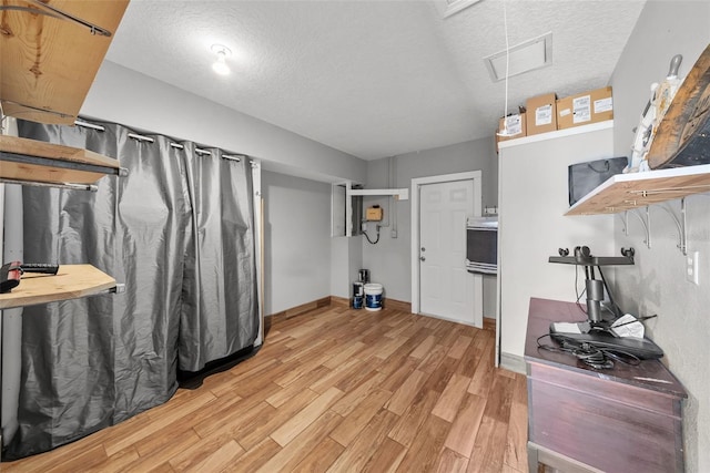 basement featuring light wood-type flooring, visible vents, and a textured ceiling