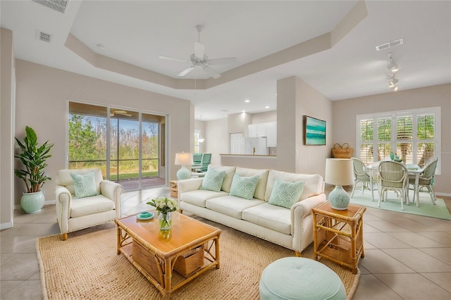 living room with ceiling fan, a wealth of natural light, a raised ceiling, and light tile patterned floors