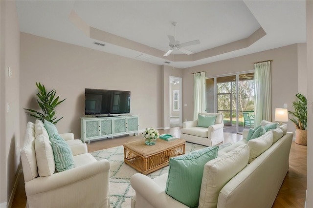 living room with ceiling fan, a raised ceiling, and light parquet flooring