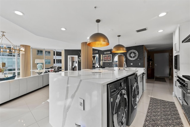 kitchen featuring pendant lighting, white cabinets, a center island with sink, and washing machine and dryer