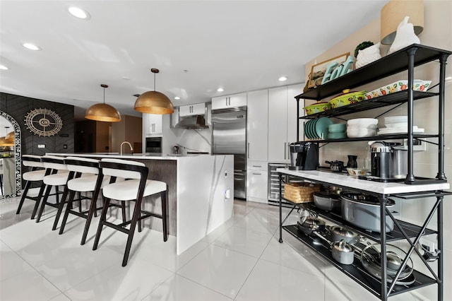 kitchen featuring light tile patterned floors, white cabinetry, built in refrigerator, decorative light fixtures, and beverage cooler