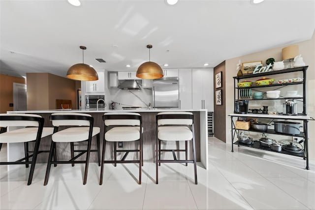 kitchen featuring pendant lighting, white cabinets, stainless steel built in refrigerator, light tile patterned floors, and a breakfast bar area