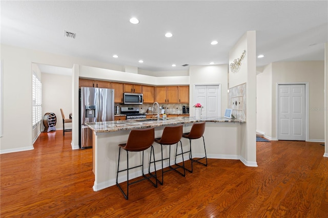 kitchen with sink, appliances with stainless steel finishes, dark hardwood / wood-style floors, kitchen peninsula, and light stone countertops