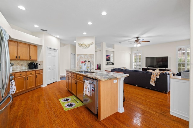 kitchen featuring sink, hardwood / wood-style flooring, stainless steel appliances, light stone countertops, and a center island with sink