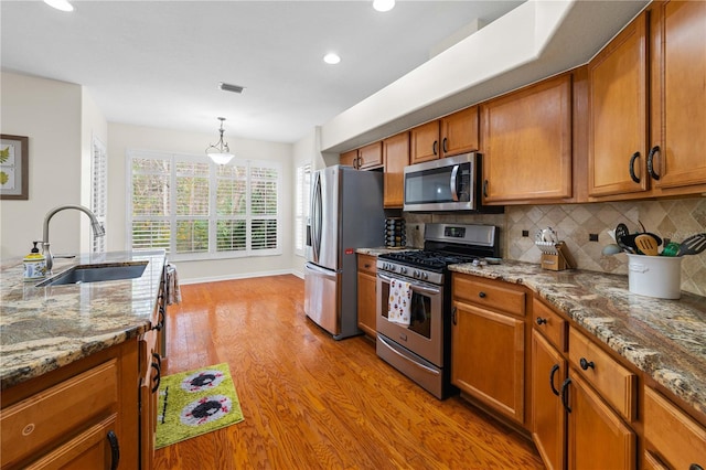 kitchen with sink, tasteful backsplash, stainless steel appliances, light stone countertops, and light hardwood / wood-style floors