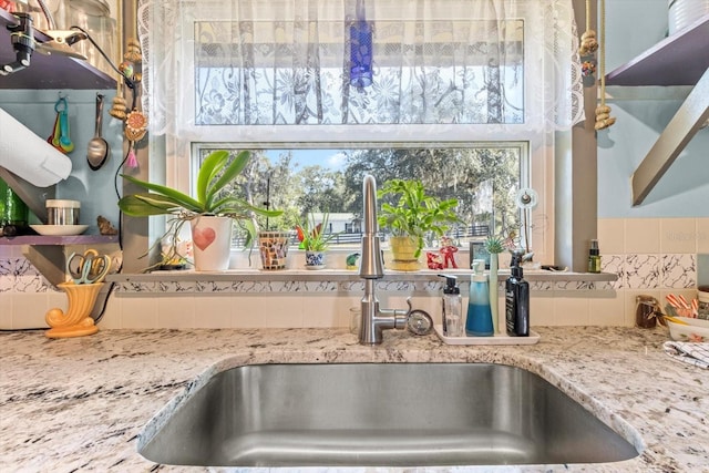 interior details with light stone countertops, sink, and backsplash