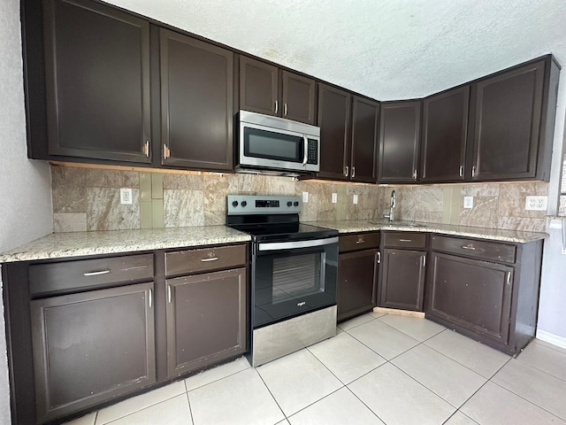 kitchen featuring light stone countertops, dark brown cabinetry, appliances with stainless steel finishes, sink, and light tile patterned flooring