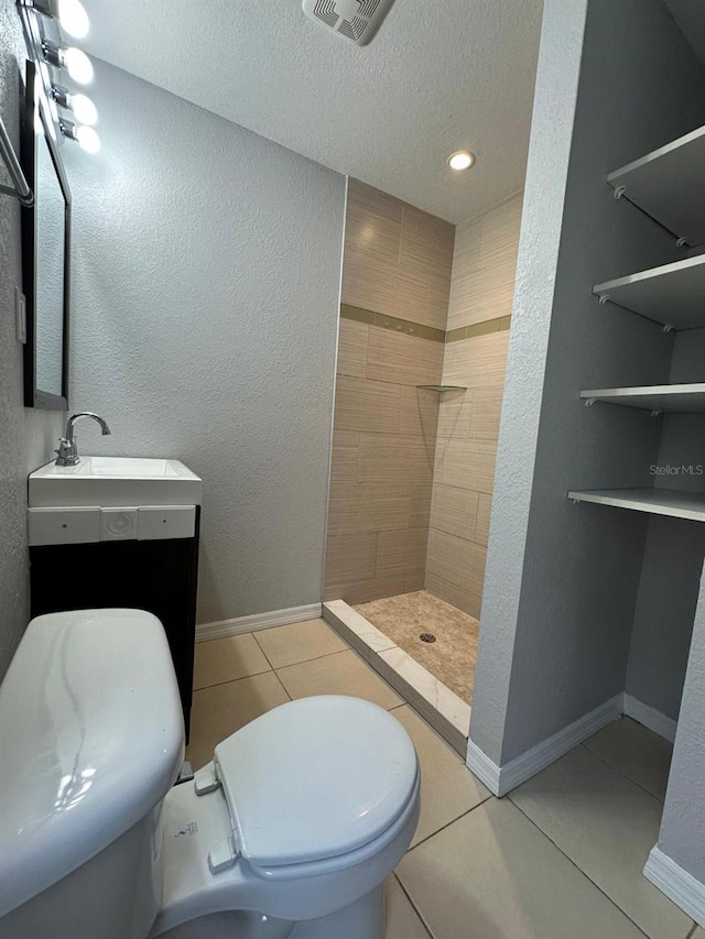 bathroom featuring toilet, a textured ceiling, tile patterned flooring, tiled shower, and vanity