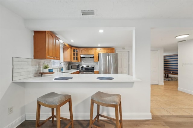 kitchen with stainless steel appliances, kitchen peninsula, light tile patterned floors, and a kitchen breakfast bar