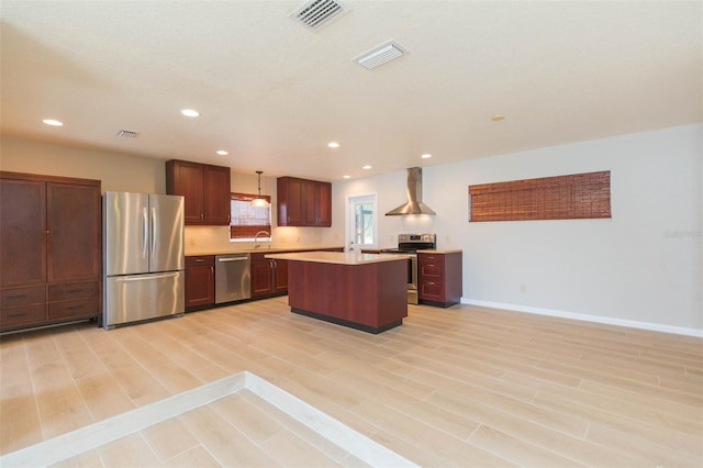 kitchen featuring a kitchen island, sink, hanging light fixtures, stainless steel appliances, and wall chimney exhaust hood