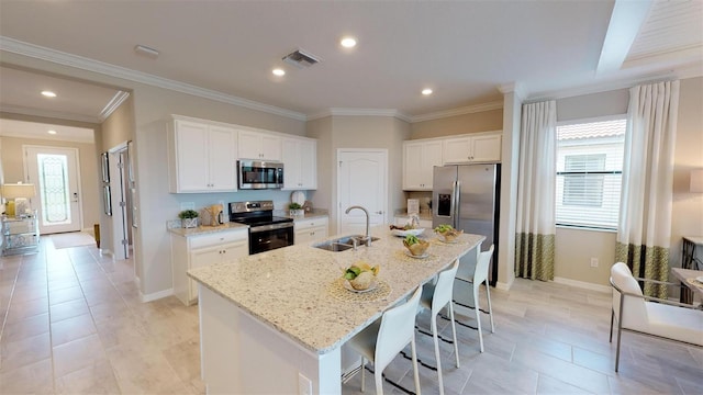 kitchen featuring appliances with stainless steel finishes, sink, white cabinets, light stone countertops, and a center island with sink