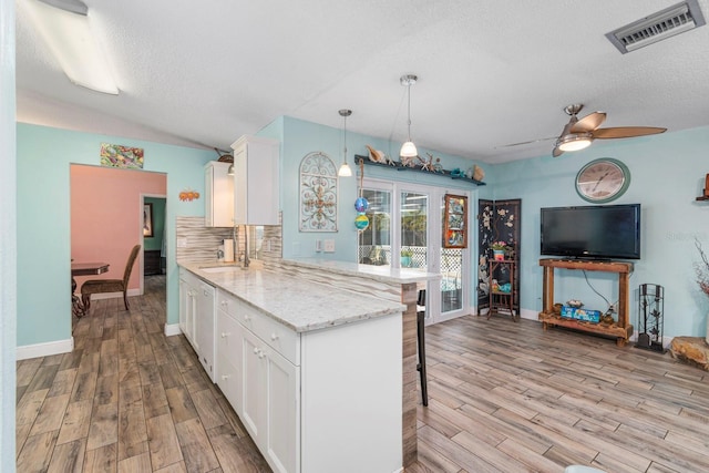 kitchen with decorative light fixtures, backsplash, light hardwood / wood-style flooring, light stone countertops, and white cabinets