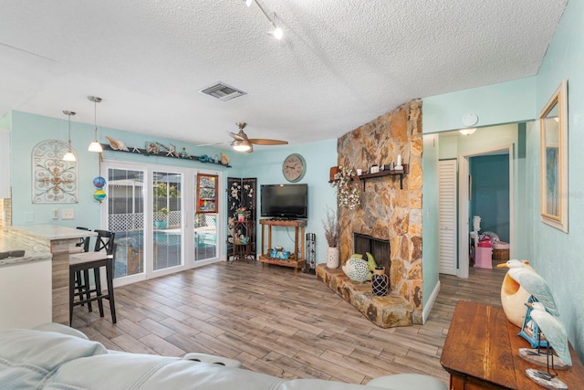 living room featuring ceiling fan, a fireplace, a textured ceiling, and track lighting