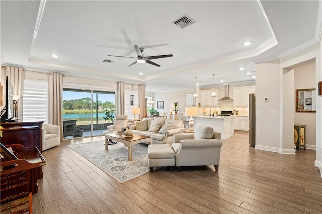 living room featuring light hardwood / wood-style flooring, ornamental molding, and a raised ceiling