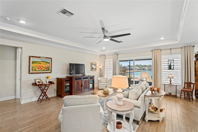 living room with a tray ceiling, ornamental molding, ceiling fan, and light wood-type flooring