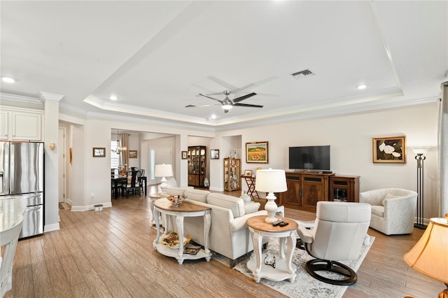 living room featuring a raised ceiling, ornamental molding, ceiling fan, and light hardwood / wood-style floors