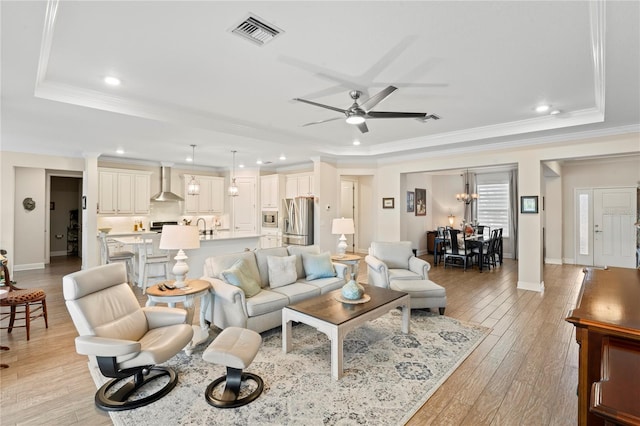 living room with a tray ceiling, ornamental molding, and light wood-type flooring