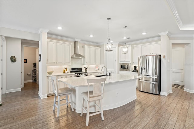 kitchen featuring a breakfast bar, hanging light fixtures, a kitchen island with sink, stainless steel appliances, and wall chimney range hood