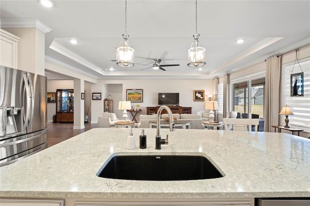 kitchen with stainless steel refrigerator with ice dispenser, a tray ceiling, light stone countertops, and sink