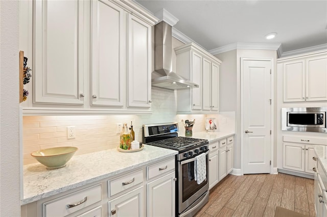 kitchen with wall chimney exhaust hood, white cabinetry, stainless steel appliances, and crown molding