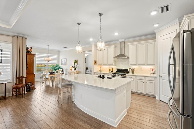 kitchen with appliances with stainless steel finishes, an island with sink, sink, light stone countertops, and wall chimney exhaust hood