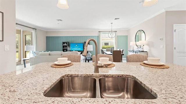 kitchen featuring light stone counters, ornamental molding, sink, and hanging light fixtures