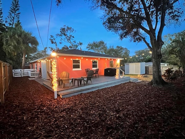 back house at dusk with a deck and a storage shed