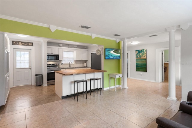 kitchen with white cabinets, butcher block countertops, appliances with stainless steel finishes, and ornate columns