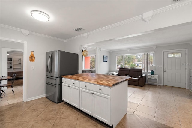 kitchen with white cabinets, butcher block counters, stainless steel fridge, light tile patterned floors, and crown molding