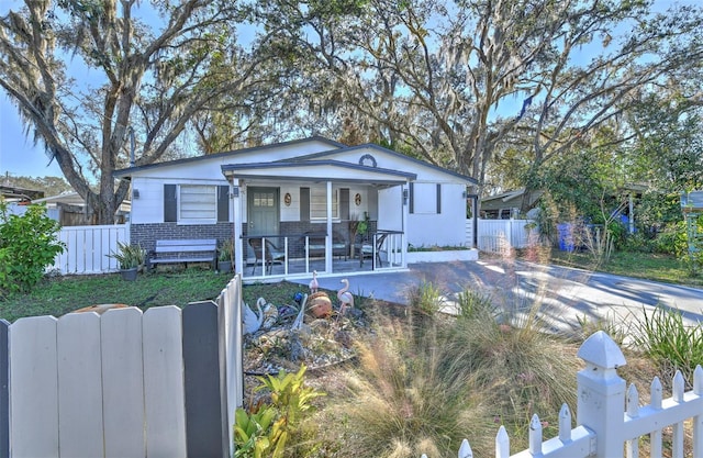 bungalow-style home with covered porch, driveway, brick siding, and a fenced front yard