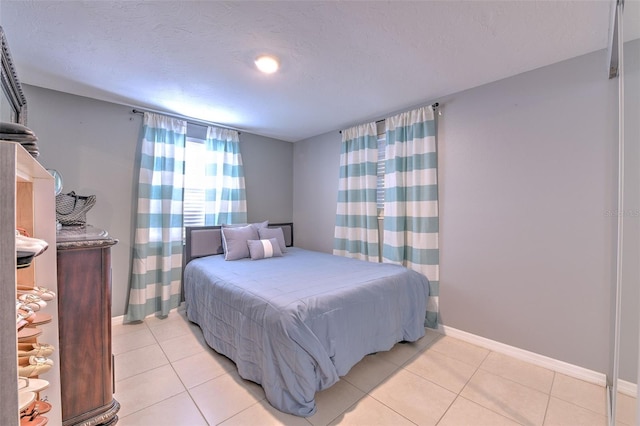 bedroom featuring light tile patterned floors, a textured ceiling, and baseboards