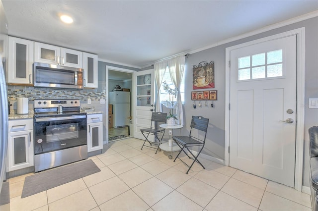 kitchen with light tile patterned floors, decorative backsplash, appliances with stainless steel finishes, ornamental molding, and white cabinetry