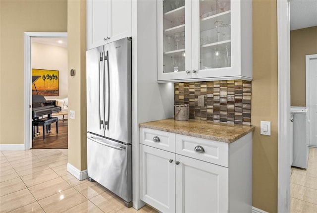 kitchen with tasteful backsplash, light tile patterned floors, stainless steel refrigerator, light stone countertops, and white cabinets