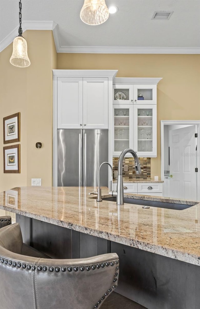 kitchen with stainless steel refrigerator, white cabinetry, ornamental molding, decorative backsplash, and decorative light fixtures