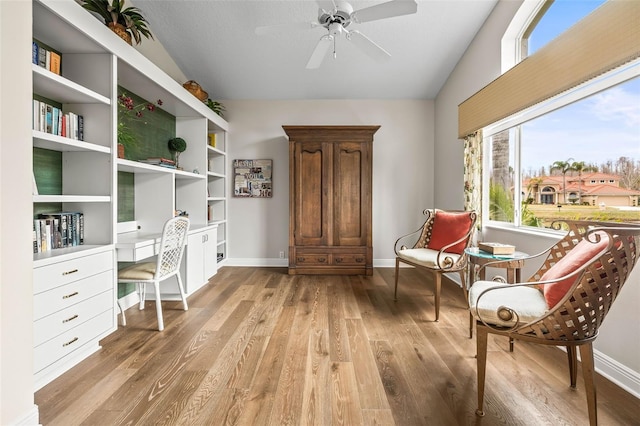 living area with ceiling fan, lofted ceiling, built in desk, and light hardwood / wood-style floors