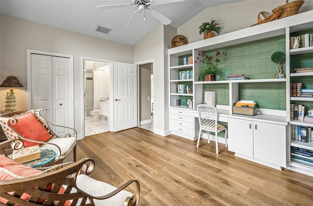 office space with ceiling fan, built in desk, vaulted ceiling, and light hardwood / wood-style flooring