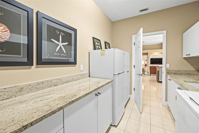 kitchen with white cabinetry, light tile patterned floors, light stone counters, and white fridge