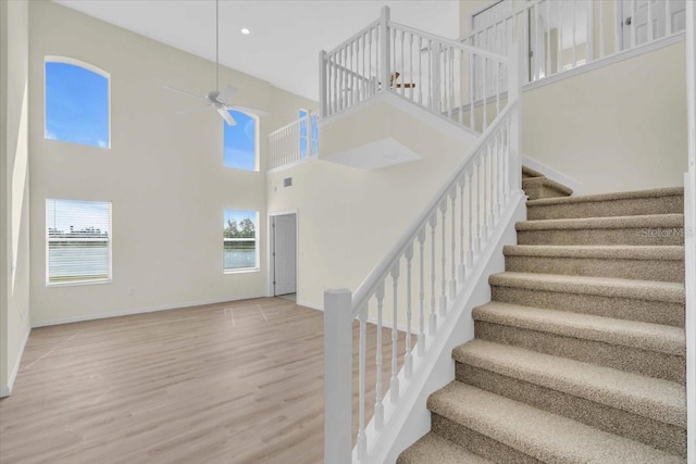 staircase with ceiling fan, a towering ceiling, and hardwood / wood-style floors