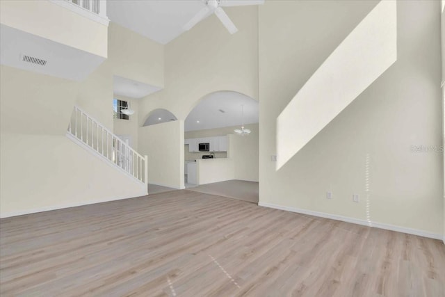 unfurnished living room with a towering ceiling, ceiling fan with notable chandelier, and light hardwood / wood-style flooring