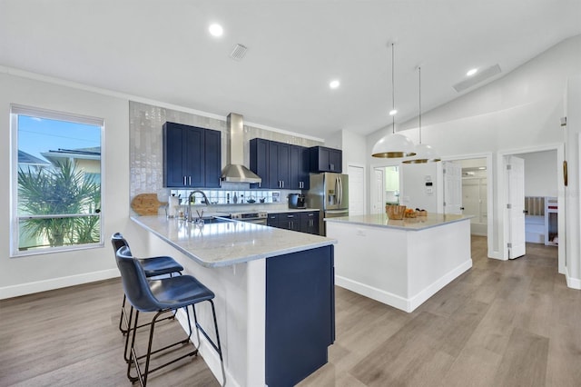 kitchen with pendant lighting, wall chimney exhaust hood, a kitchen bar, stainless steel fridge, and kitchen peninsula