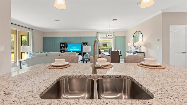 kitchen with sink, ornamental molding, light stone countertops, and hanging light fixtures